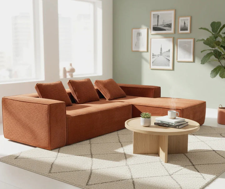 Modern rust-colored sofa with three cushions and round wood coffee table in bright living room