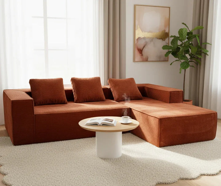 Modern rust-colored sectional sofa with three cushions, round coffee table, and indoor plant in a bright living room