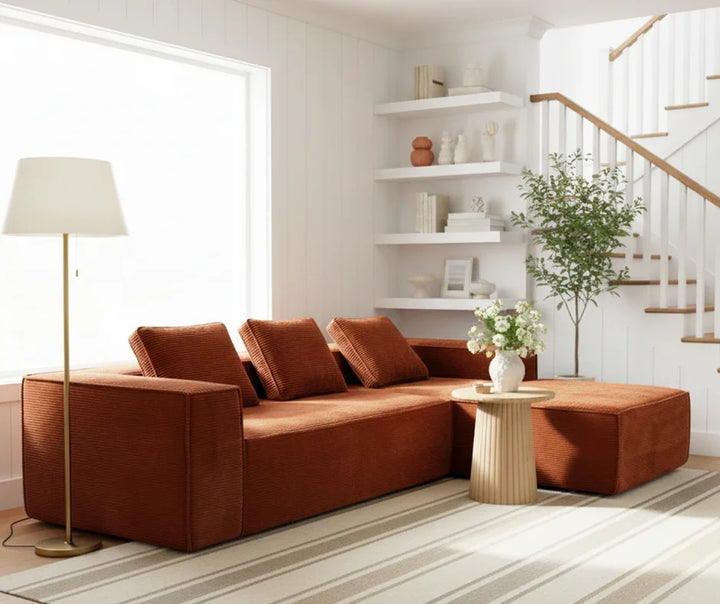 Modern living room with a rust-colored sectional sofa, floor lamp, round coffee table, and decorative plant