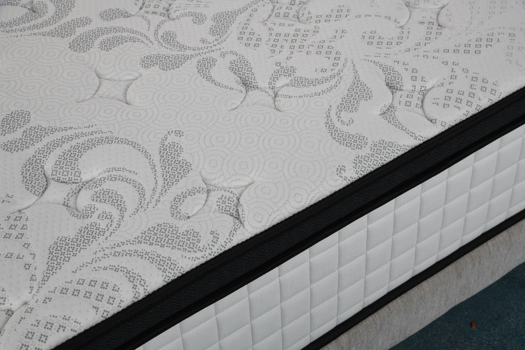 Close-up of a patterned, quilted mattress with black trim on a bed frame