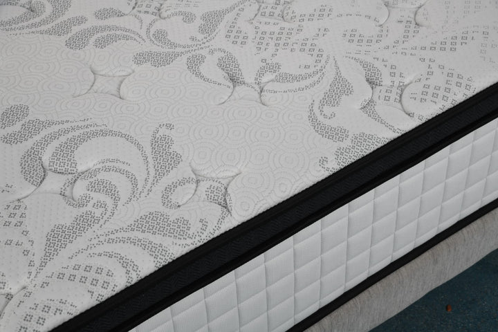 Close-up of a patterned, quilted mattress with black trim on a bed frame
