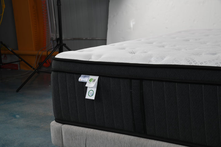 Close-up of a modern mattress with white quilted top and black sides on a grey bed base