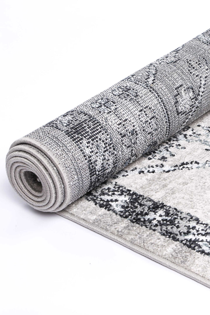 Rolled grey area rug with distressed black pattern on white background
