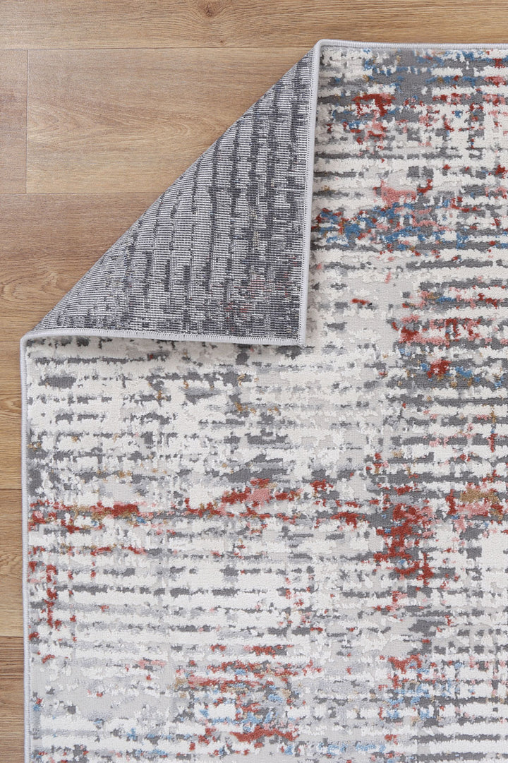 Modern abstract area rug with gray, red, and blue pattern on wood floor, corner flipped.