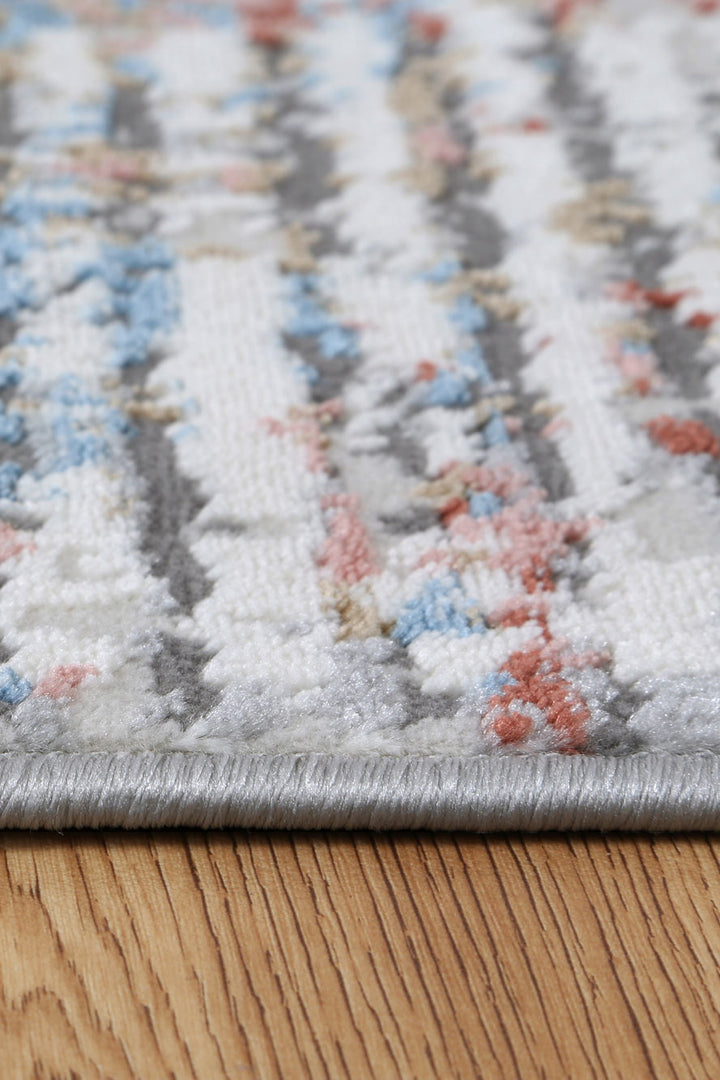 Close-up of a multicolor patterned area rug with grey, blue, and coral tones on wood floor