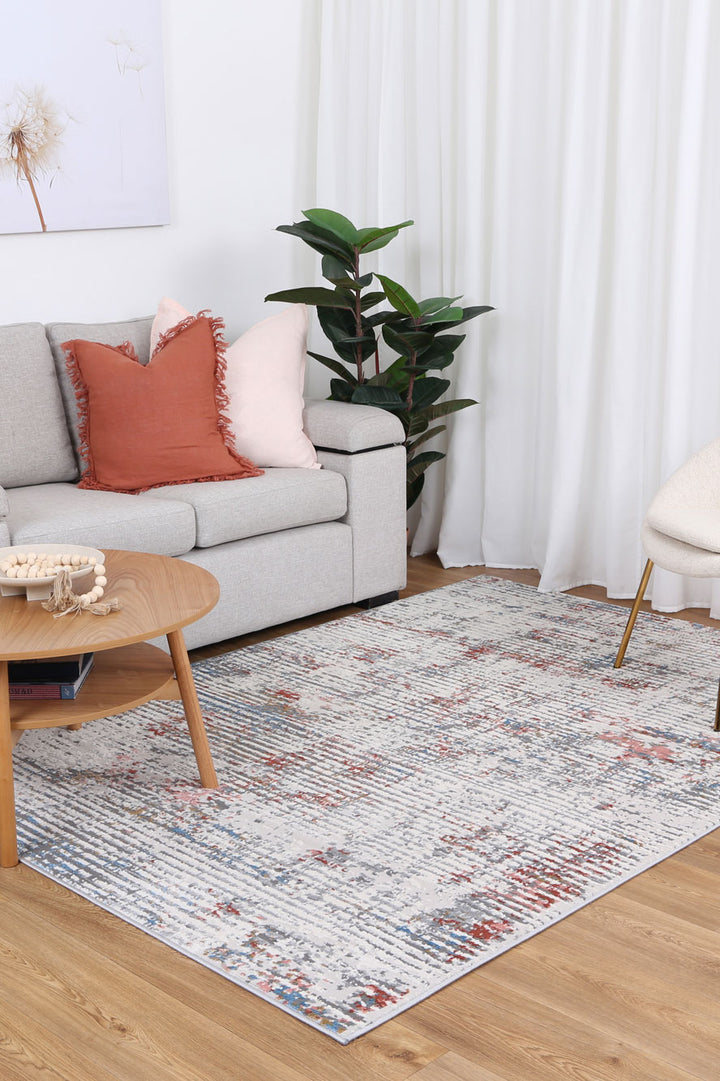 Modern living room with light gray sofa, accent pillows, patterned area rug, and wooden coffee table