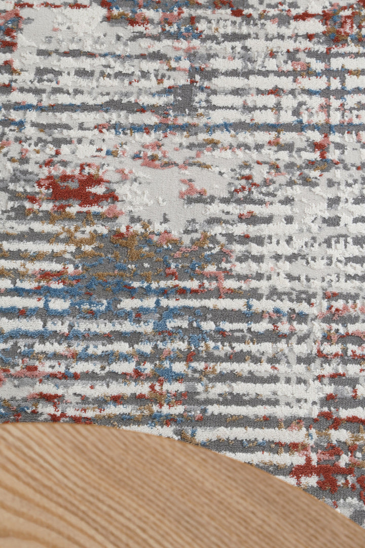 Modern abstract area rug with gray, white, red, blue, and gold pattern beside wood table