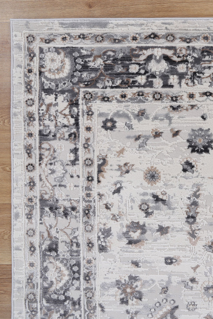 Corner of a traditional area rug with floral grey and beige patterns on wood floor