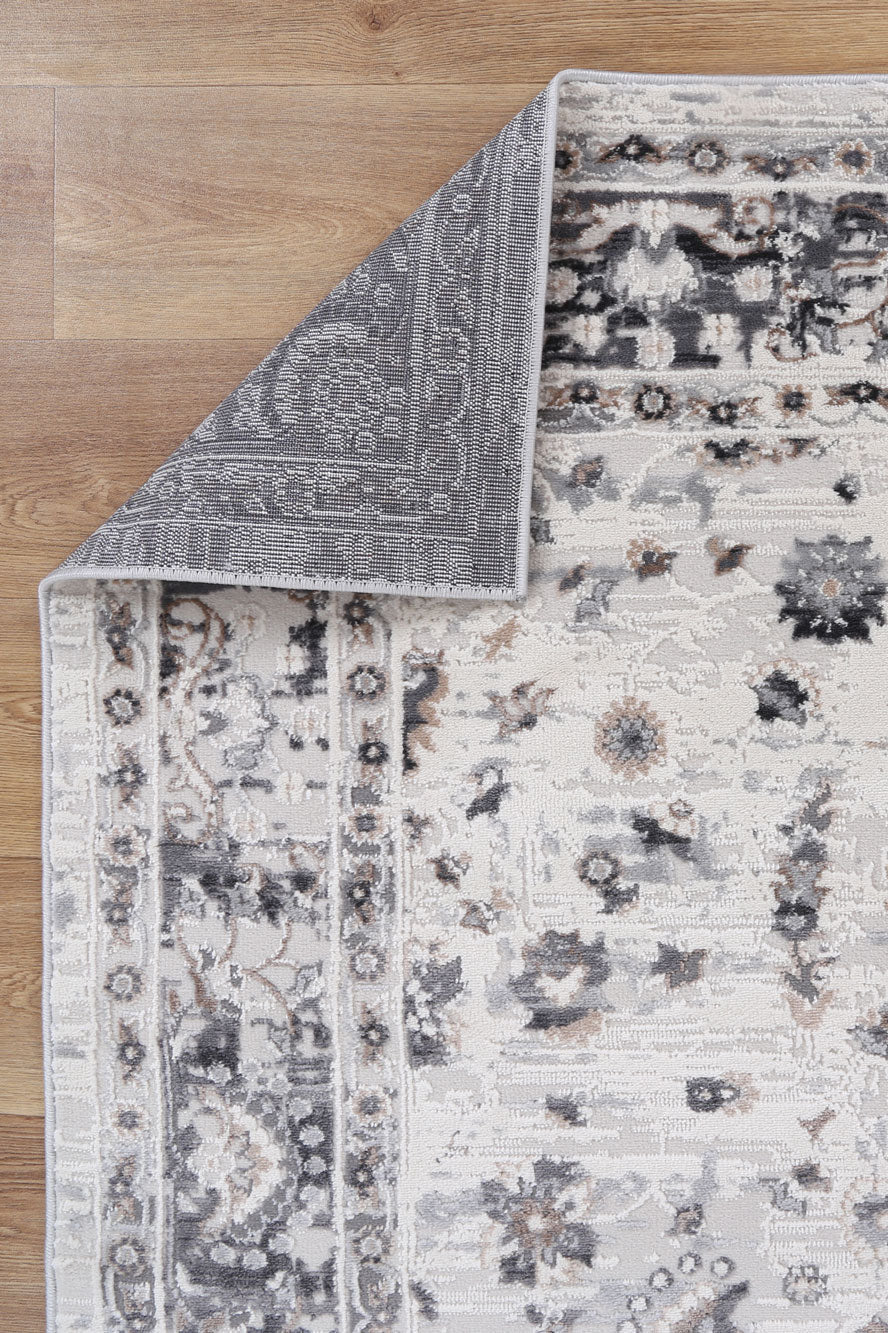 Corner of a patterned area rug with floral design on wooden floor