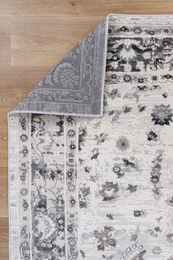 Corner of a patterned area rug with floral design on wooden floor
