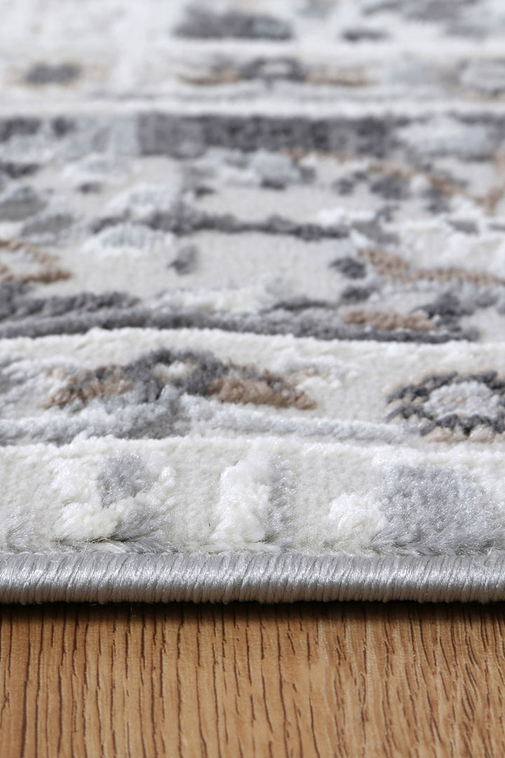 Close-up of textured area rug with grey, white, and beige patterns on wooden floor