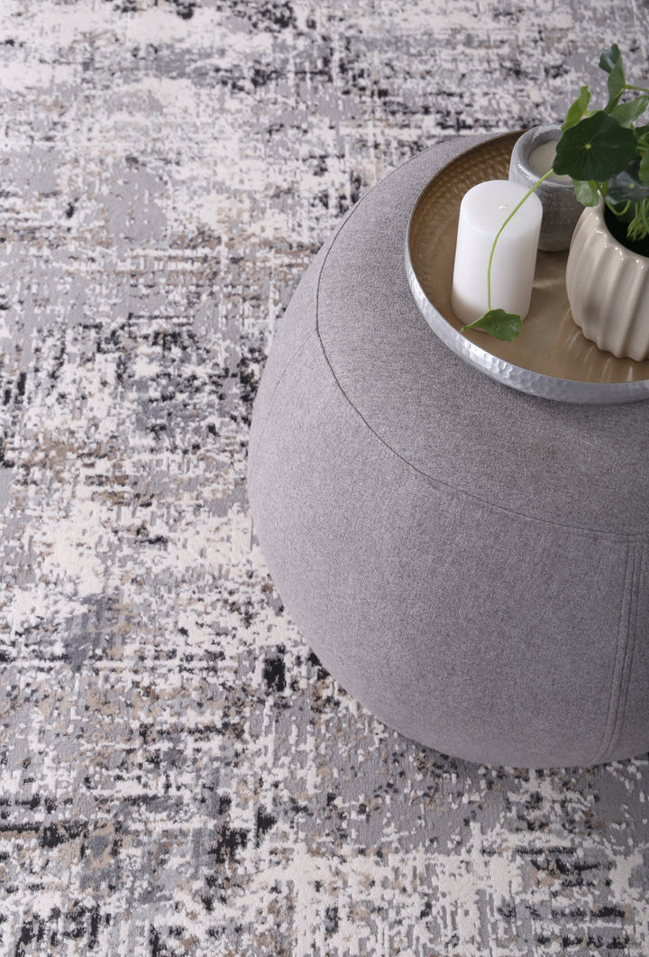 Modern round gray ottoman on abstract area rug with decorative tray, candle, and plant