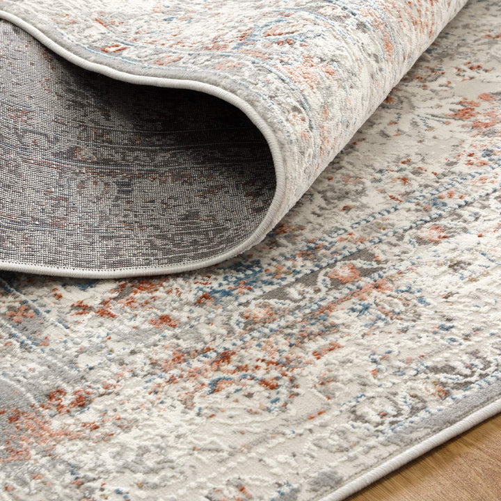 Close-up of a modern area rug with gray, blue, and rust abstract patterns on hardwood floor