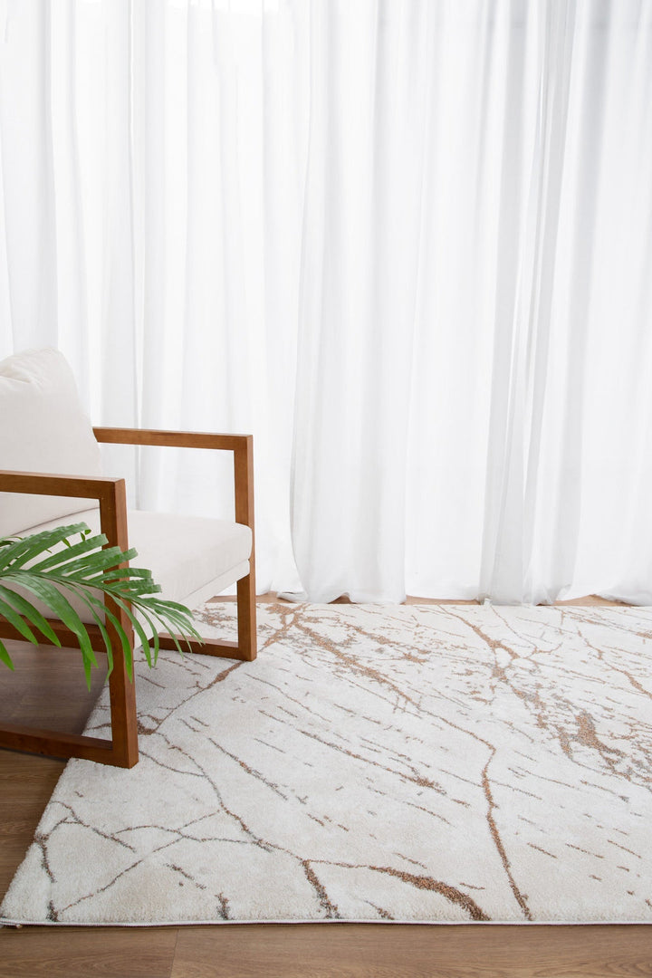 Modern living room with white fabric armchair, wood frame, abstract area rug, and green plant