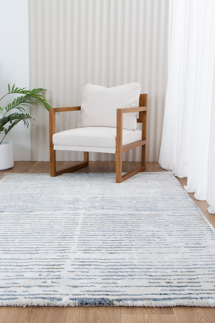 Modern wooden armchair with white cushions on a striped area rug in a bright living room