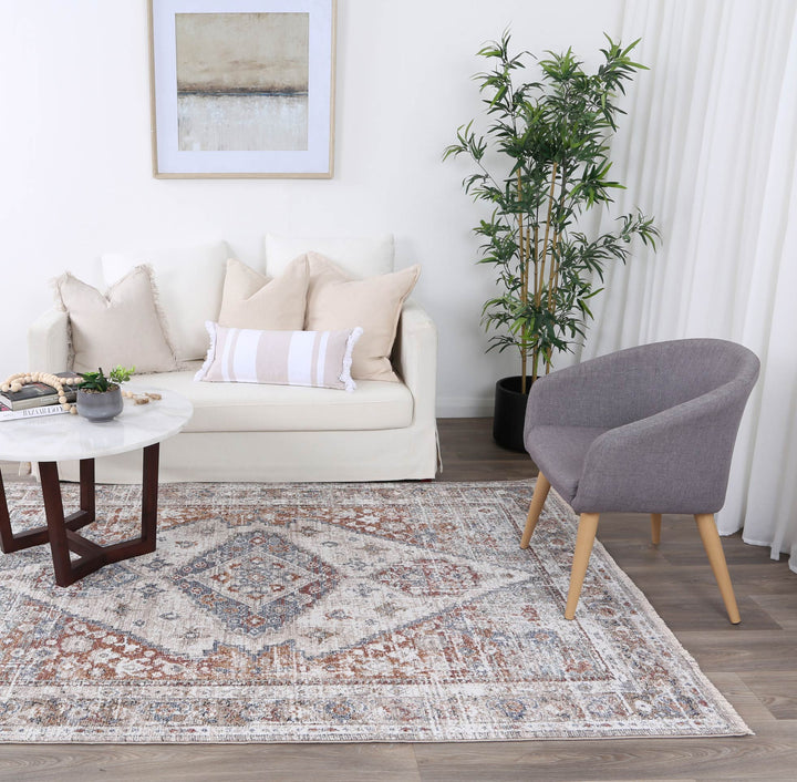 Modern living room with cream sofa, accent pillows, round coffee table, patterned area rug, gray armchair, and potted plant