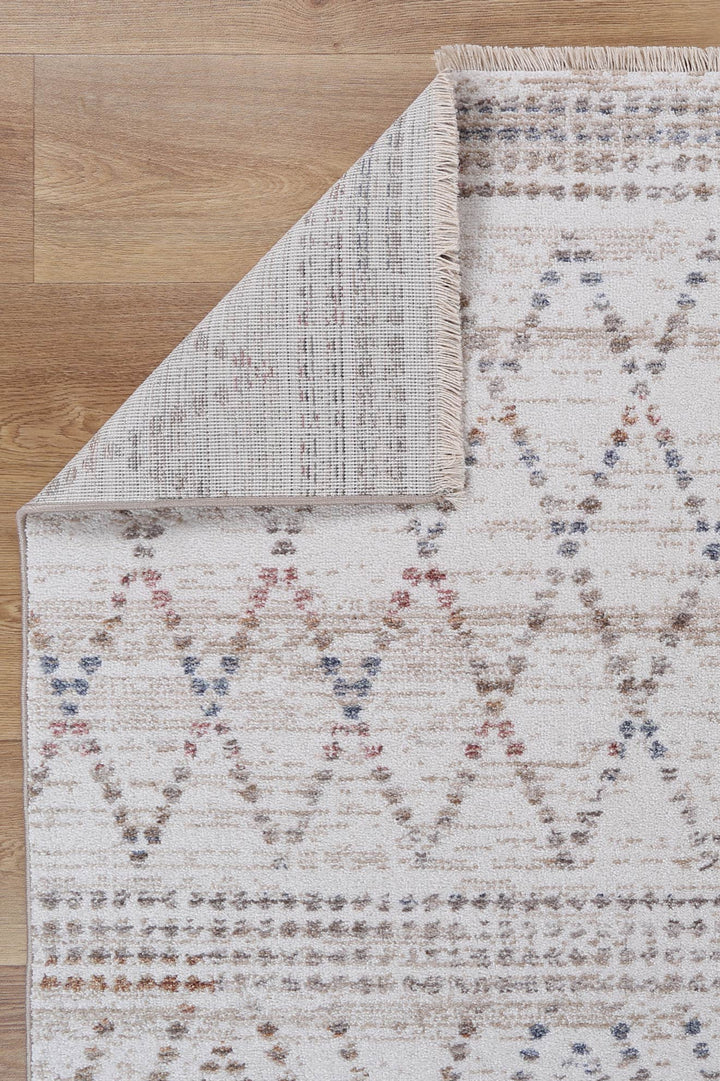 Beige patterned area rug with geometric design on wooden floor, corner folded