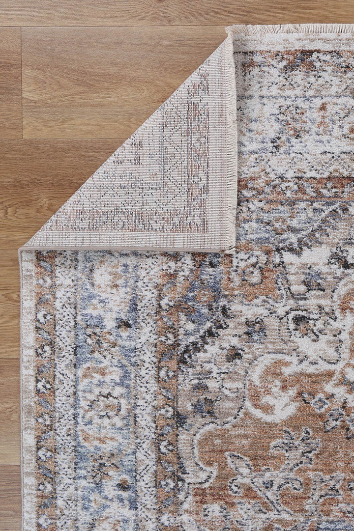 Corner of a vintage-style area rug with intricate beige, blue, and brown patterns on wood floor