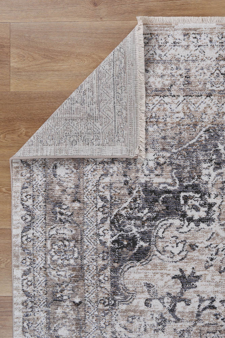Vintage style area rug with distressed floral pattern on wood floor, corner flipped up