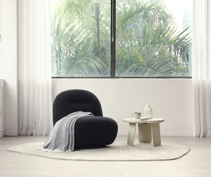 Modern black accent chair with throw blanket and round coffee table in bright living room