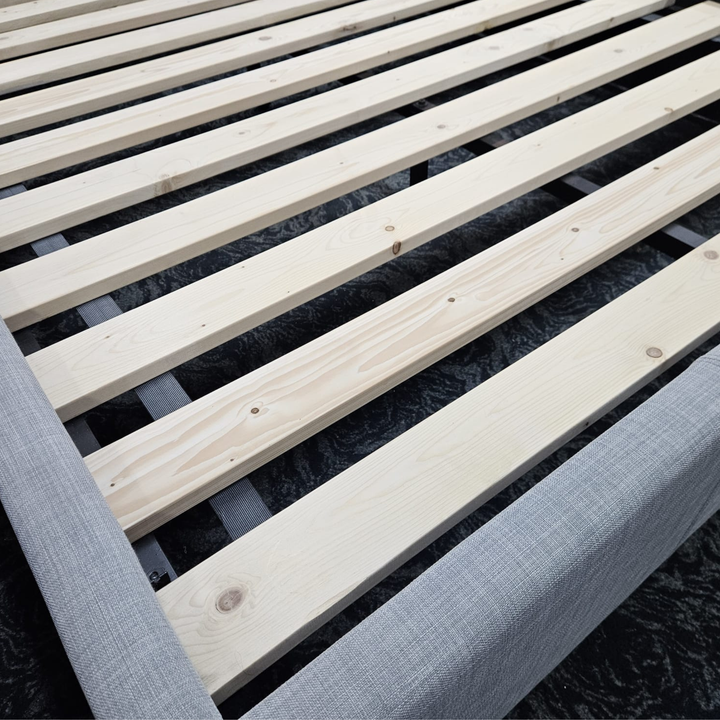 Wooden slatted bed frame with light fabric upholstery, close-up view