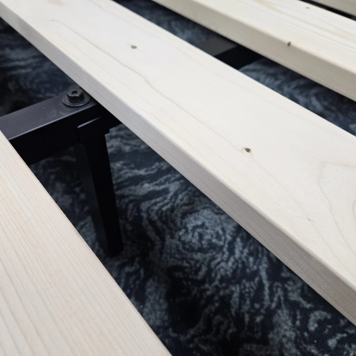 Close-up of wooden bed slats on a black metal frame above a patterned carpet
