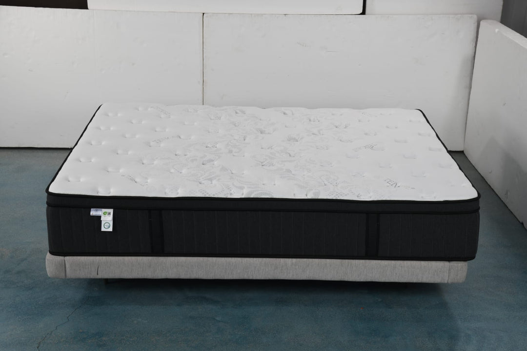 Plush white and black mattress with textured top on a light grey bed base in a minimalist room