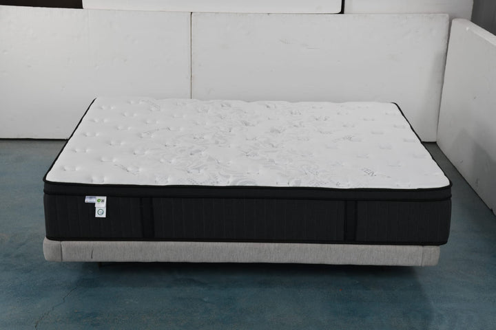 Plush white and black mattress with textured top on a light grey bed base in a minimalist room