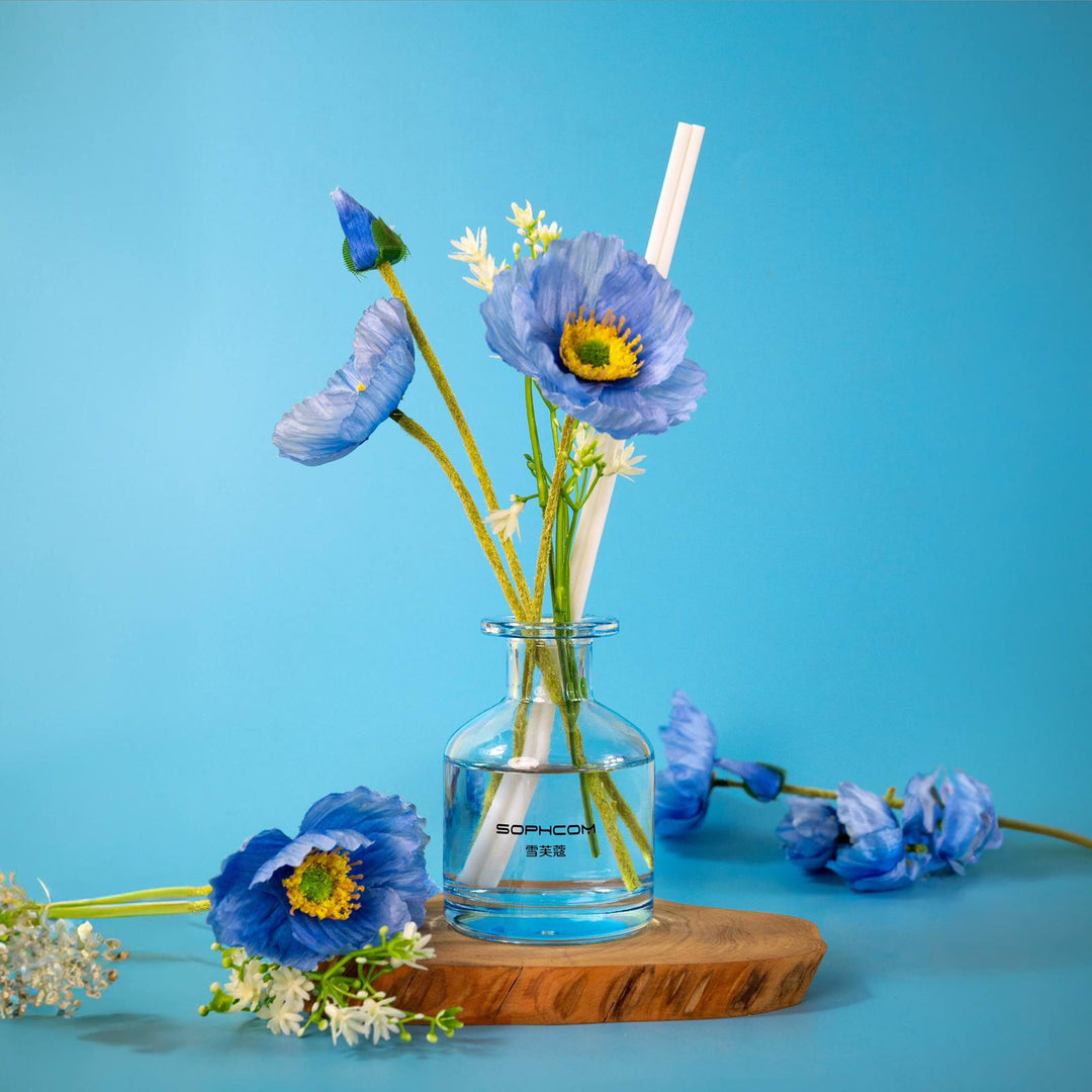 Blue poppy flowers in a glass vase on wooden tray, minimalist home decor on blue background.