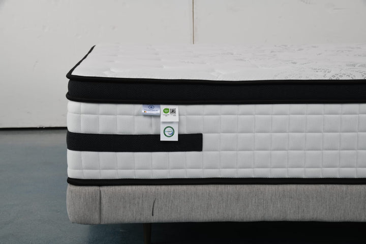 Close-up of a modern hybrid mattress with quilted white and black cover on a bed base