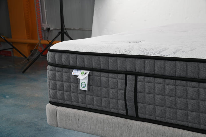 Gray quilted mattress with white top on fabric bed frame in modern room setting