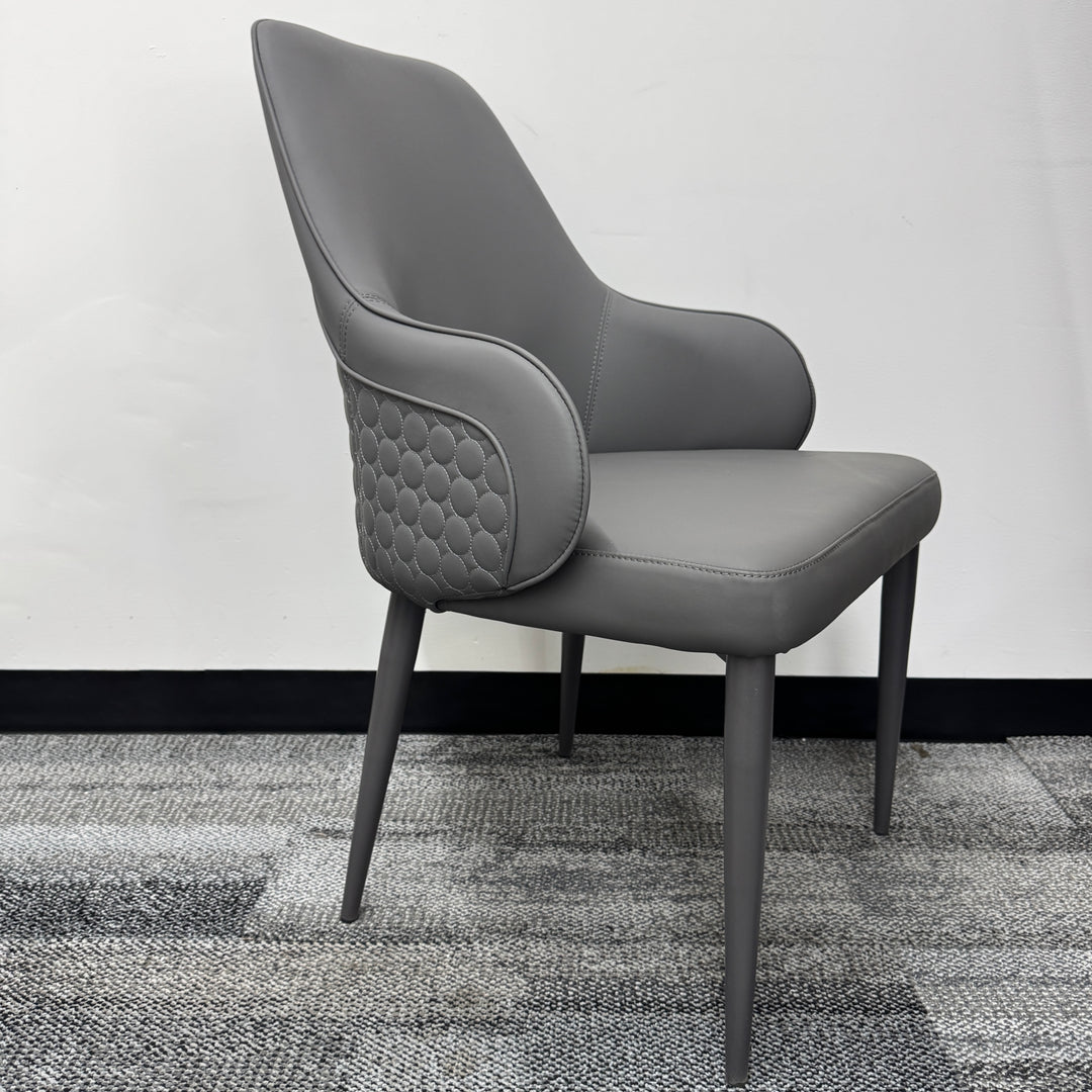 Modern grey upholstered armchair with quilted sides, minimalist design, on carpeted floor
