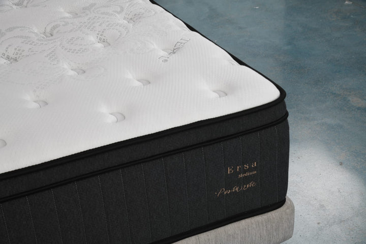 Close-up of a medium firmness mattress with white quilted top and black sides on a bed base