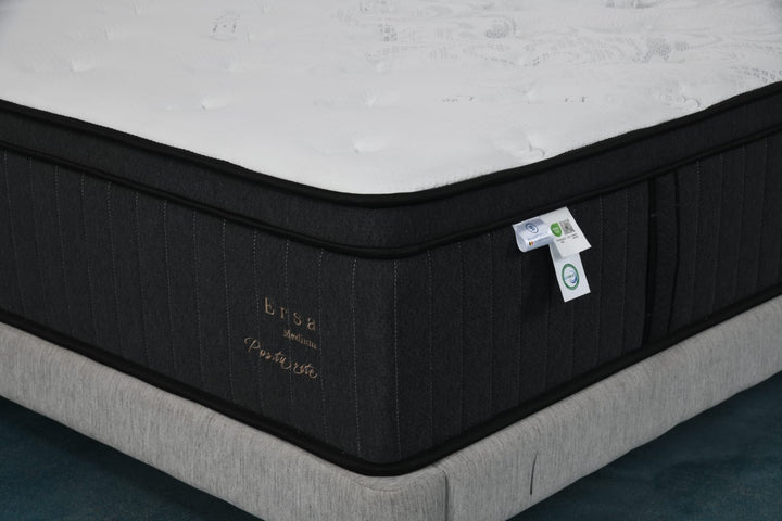 Close-up of a medium-firm mattress with a white quilted top and black sides on a bed base