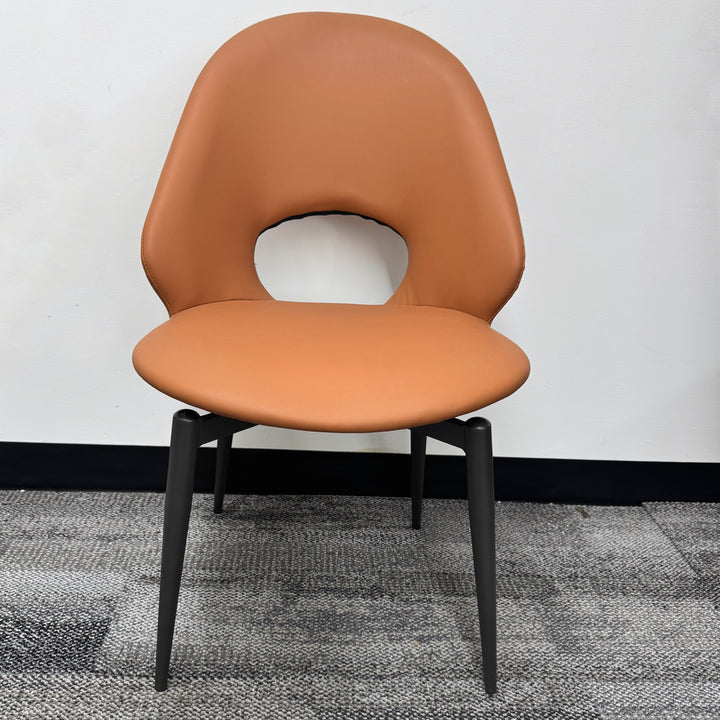 Modern tan accent chair with a round cutout back and black metal legs on a gray carpet
