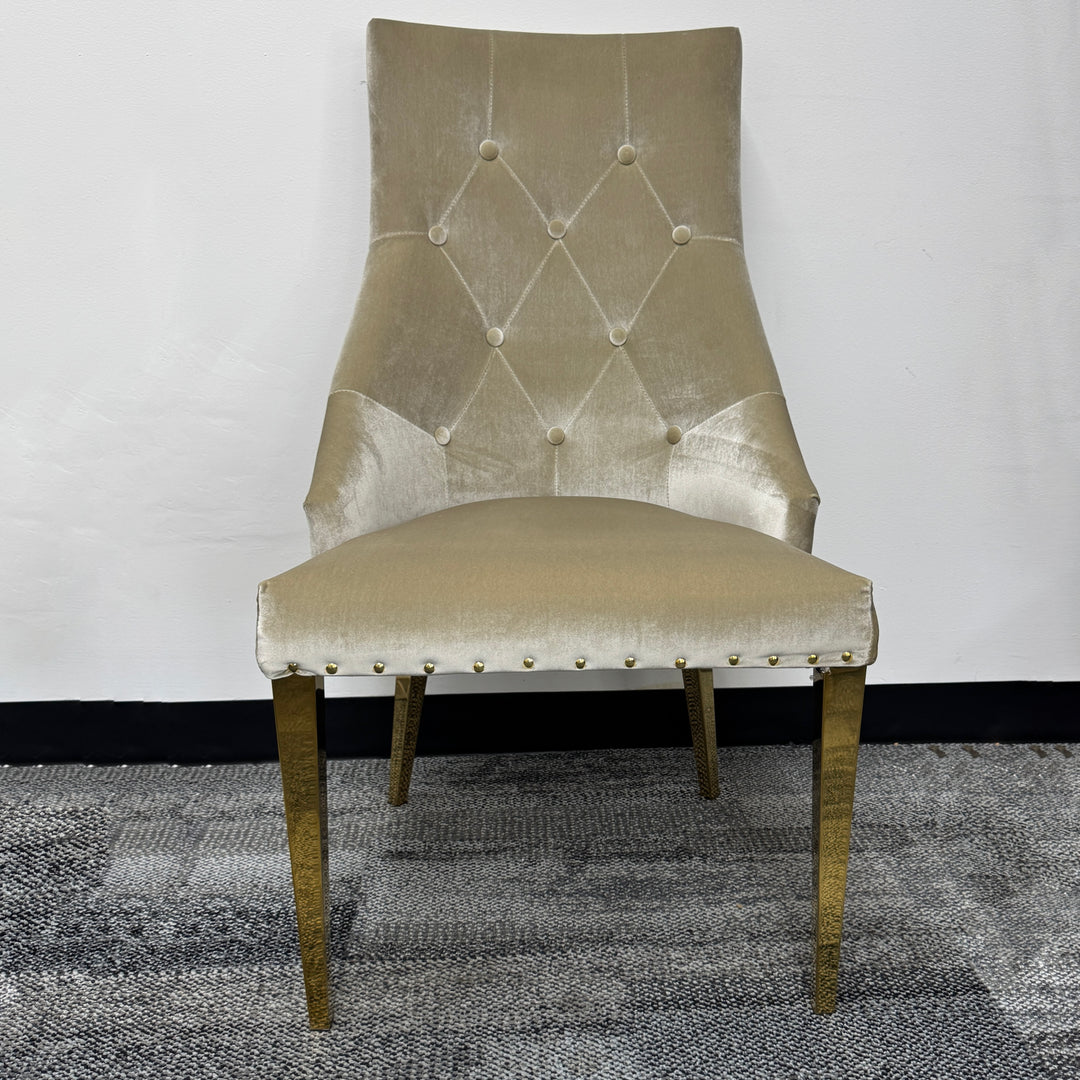 Beige velvet upholstered dining chair with gold legs and button-tufted backrest on carpet