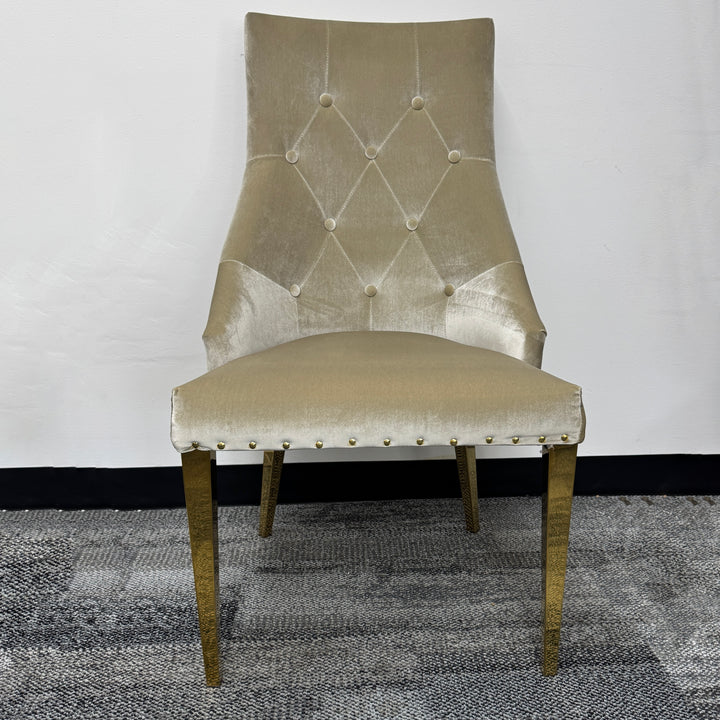 Beige velvet upholstered dining chair with gold legs and button-tufted backrest on carpet