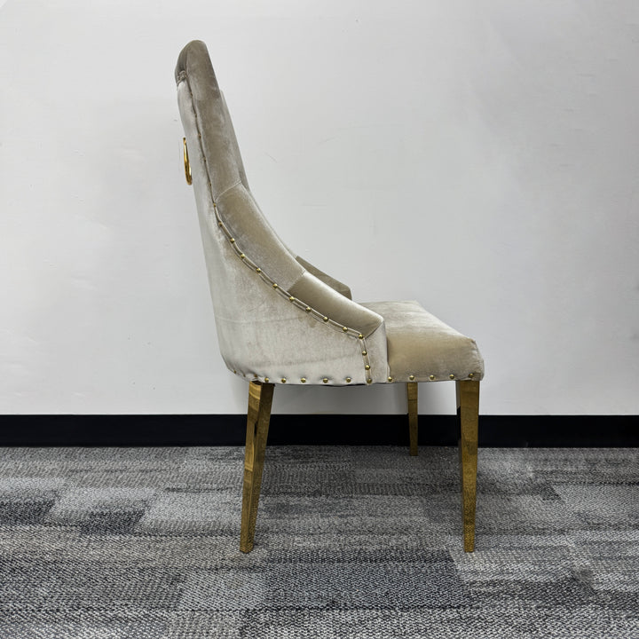 Beige velvet accent chair with gold legs and stud detailing, side view on carpet